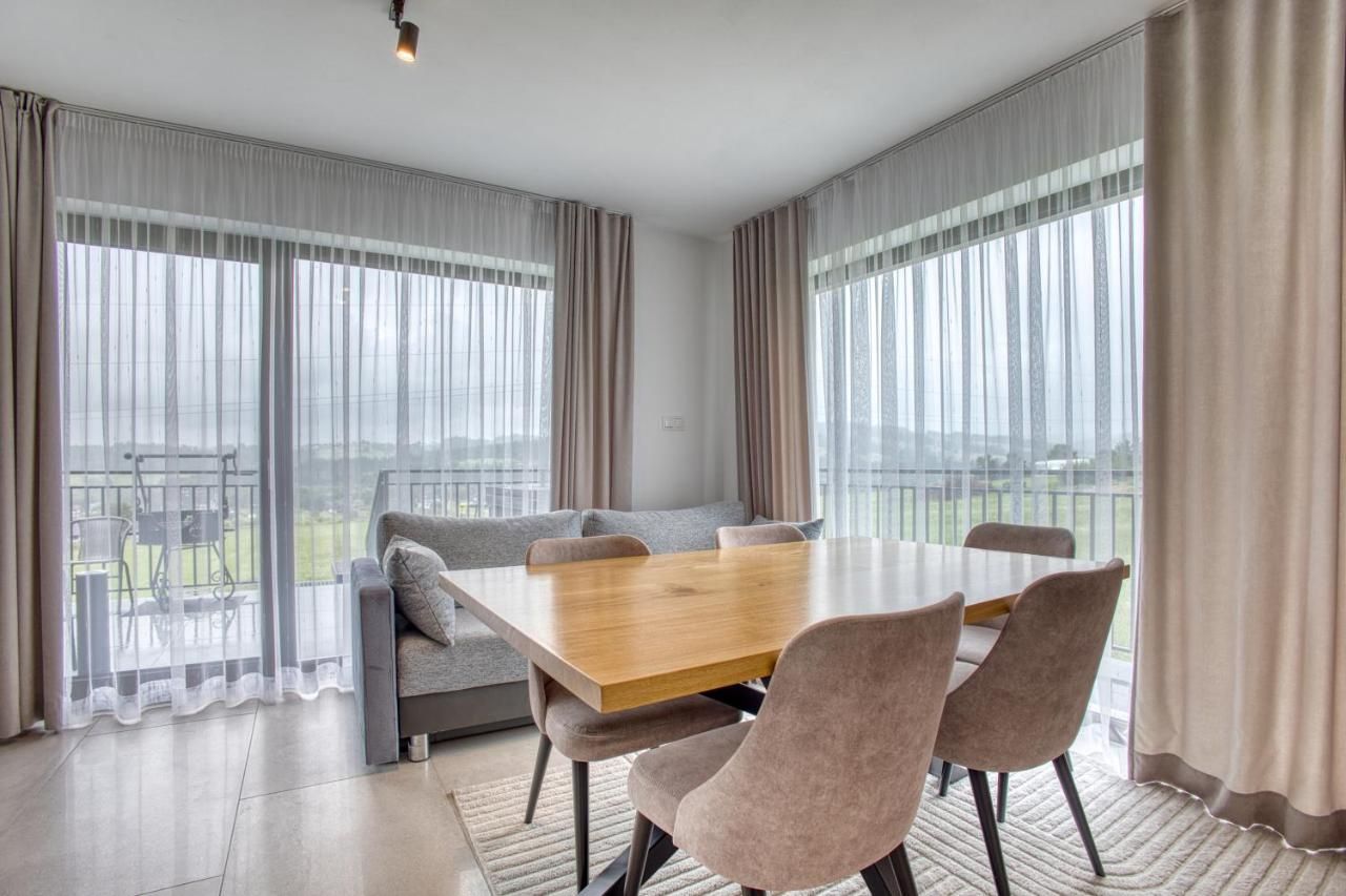 Jadalnia z drewnianym stołem, szarą sofą i dwoma dużymi oknami na balkon